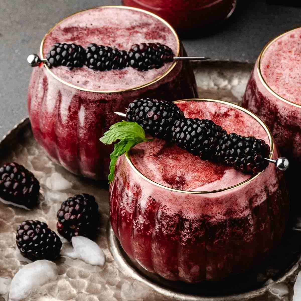 Blackberry witches brew Halloween drink in a round pumpkin-style glass topped with fresh blackberries and mint