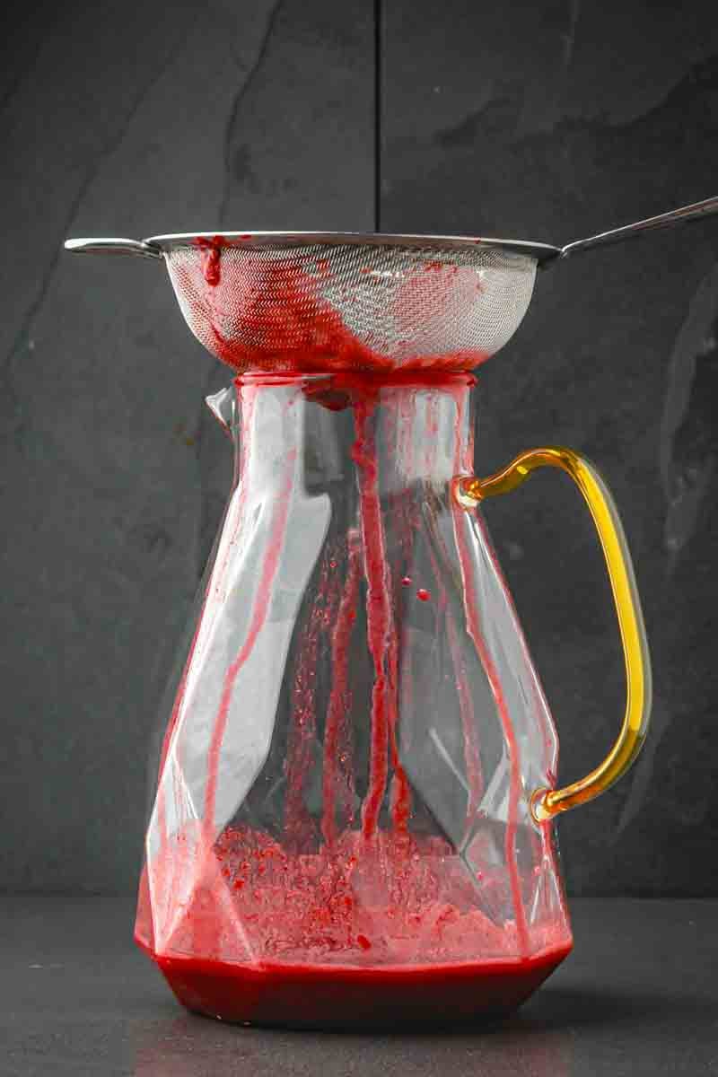 Blackberry mixture being pressed through a fine-mesh strainer into a pitcher