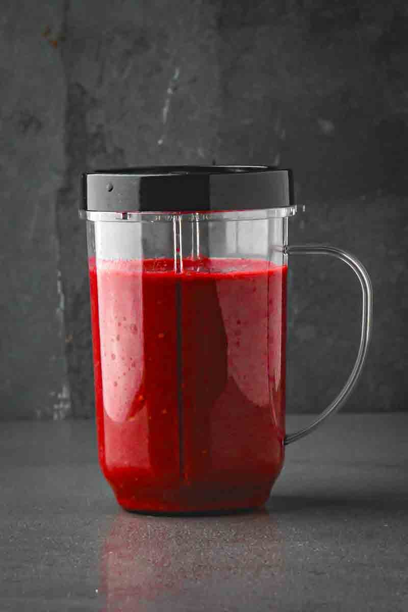 Pitcher of blackberry witches brew next to filled pumpkin-style glasses with mint and blackberry garnish