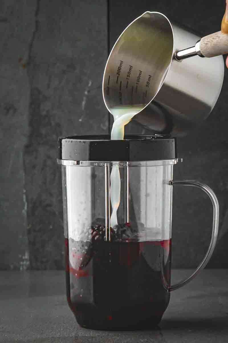 Sparkling water being stirred into the purple blackberry base in a pitcher