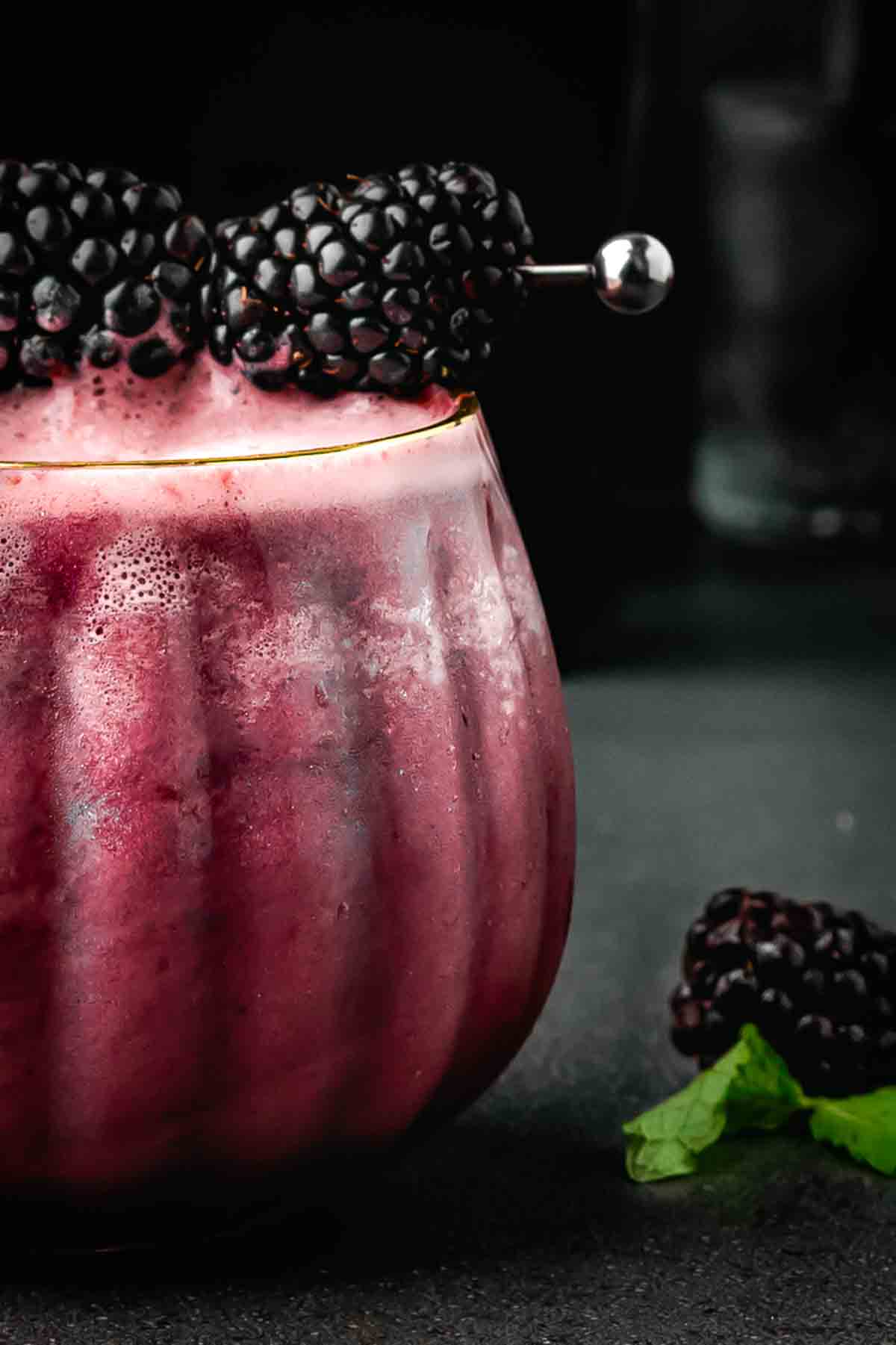 Fizzy purple Halloween mocktail in a round pumpkin glass with blackberries on top