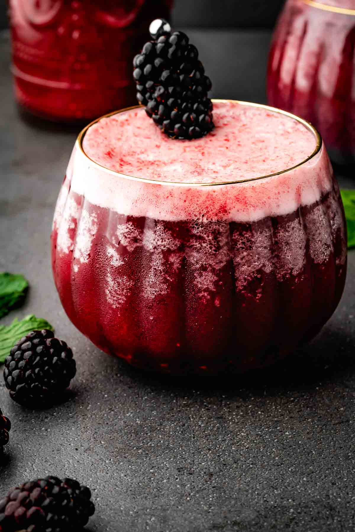 Fizzy dark burgundy Halloween mocktail in a round pumpkin glass with blackberries on top